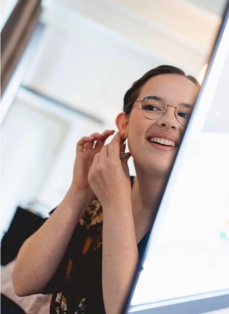 Femme souriante mettant une boucle d’oreille après un cours de maquillage personnalisé réalisé par une maquilleuse professionnelle.