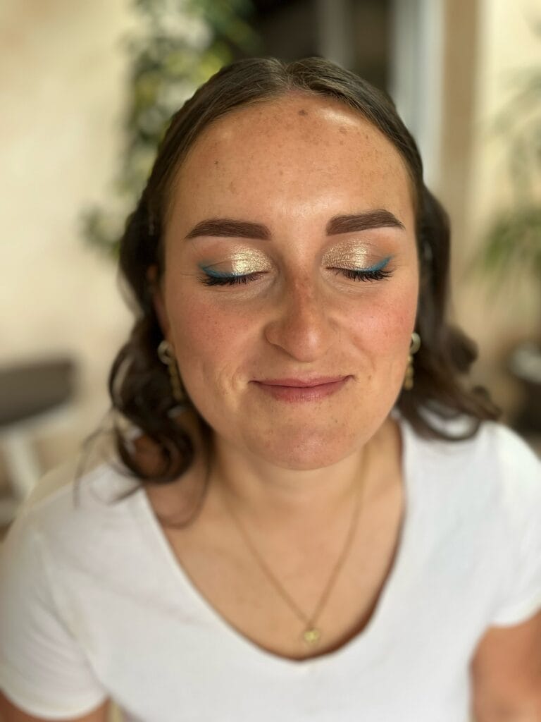 Maquillage invité avec fard doré lumineux et eyeliner bleu sur femme aux yeux fermés.
